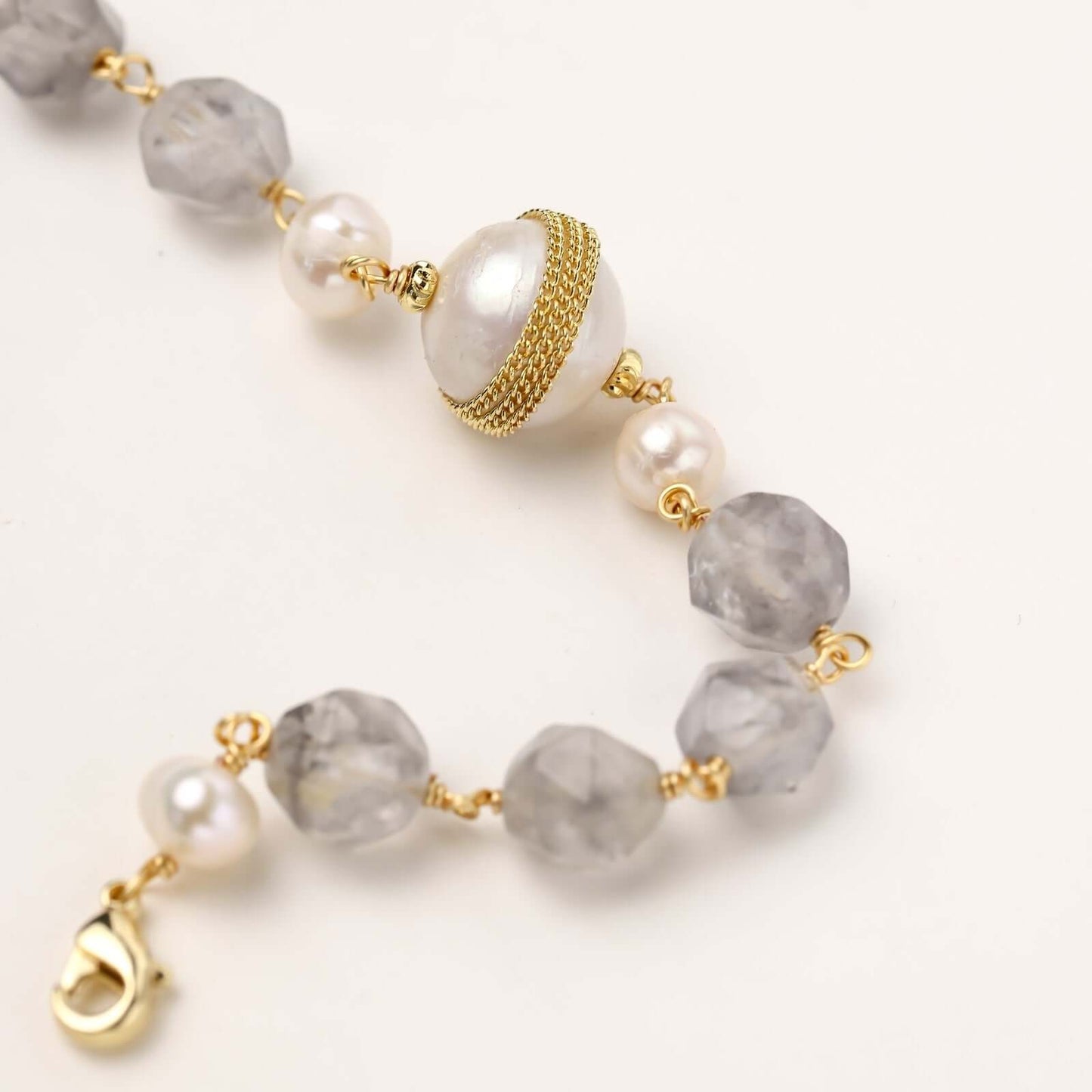 Gold-plated bracelet with white freshwater pearls and translucent grey crystals, featuring mesh-wrapped baroque pearl centerpiece
