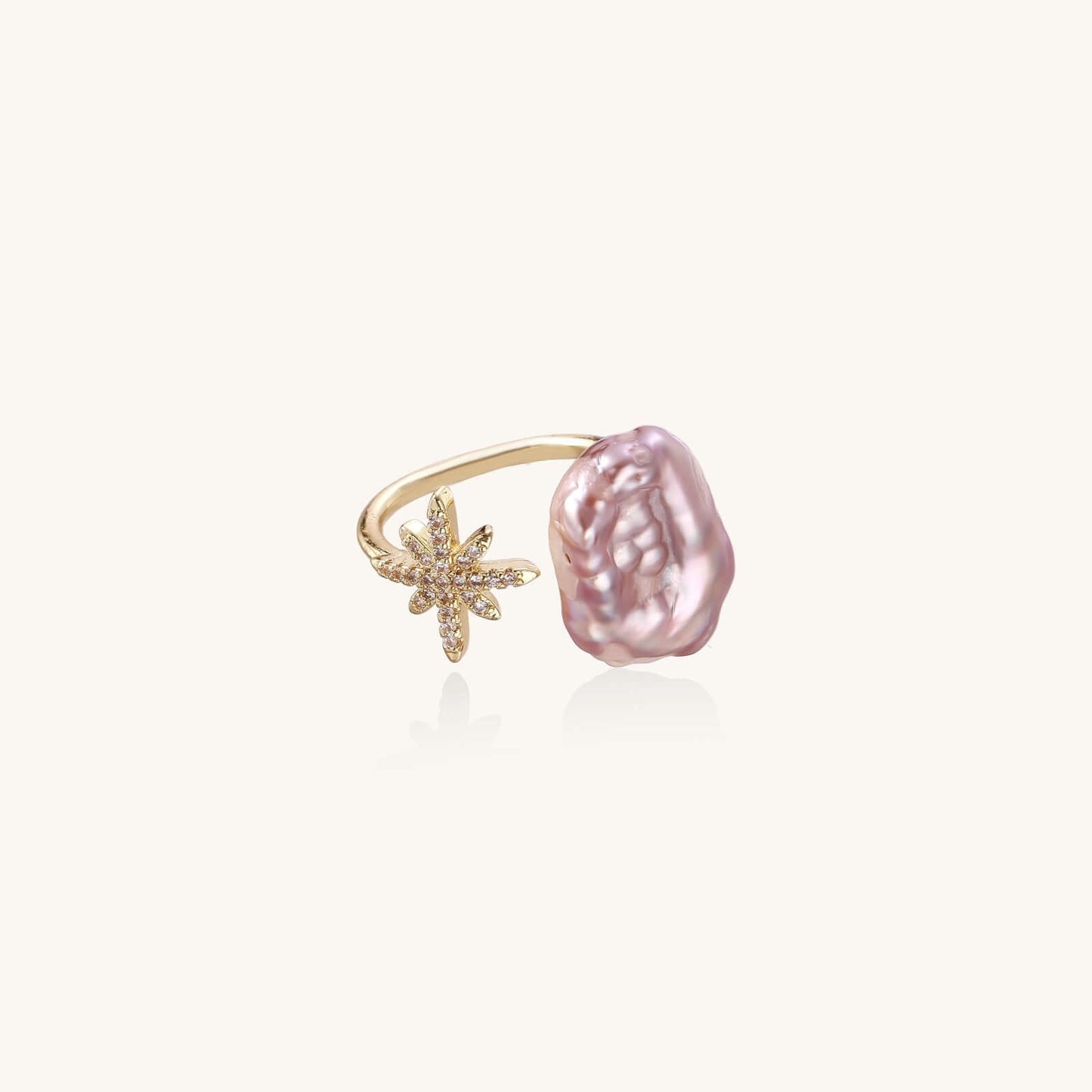 Adjustable ring with lavender baroque pearl and crystal star charm on gold-plated band against cream background.