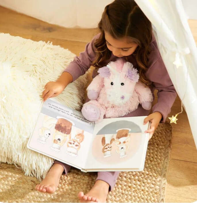 Child reading a book while holding a plush Microwavable Plush Unicorn for comfort and relaxation.