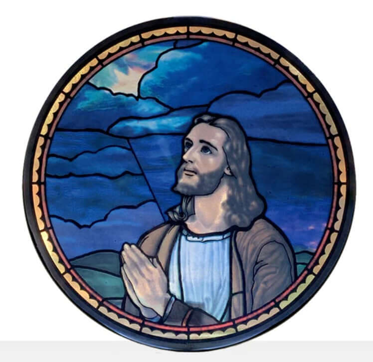 A stained glass window depicting Jesus in prayer with a blue sky background.