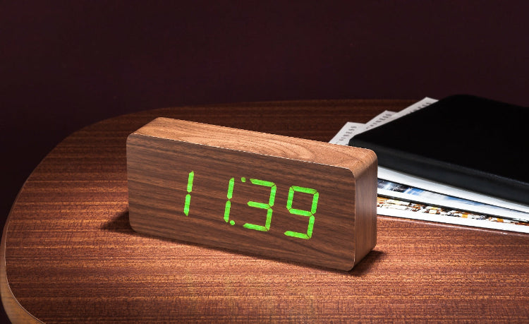 A sleek wooden alarm clock displaying the time in green LED numerals placed on a wooden surface.