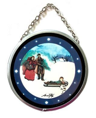 A round stained glass Christmas ornament featuring a vintage winter scene with a sleigh ride, two figures, and a child on a sled, with a chain for hanging.