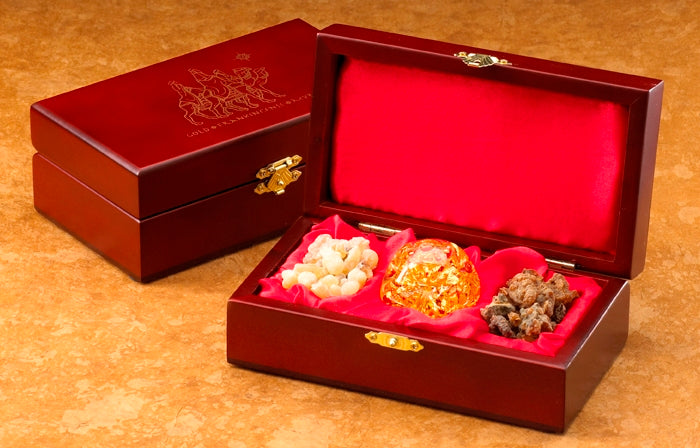 A deluxe wooden box set containing a hand-blown glass globe with real 23k gold, along with authentic frankincense and myrrh, displayed on a red satin lining.