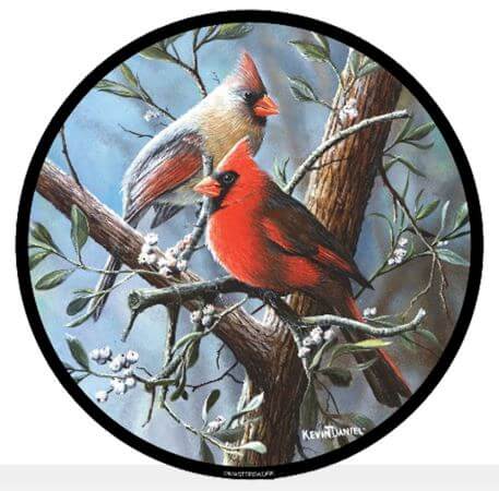 A round stained glass panel featuring artistic depictions of a male and female cardinal perched on a branch with leaves and a blue sky in the background.