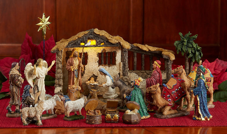 Nativity scene with figures and stable on a red surface with poinsettias.
