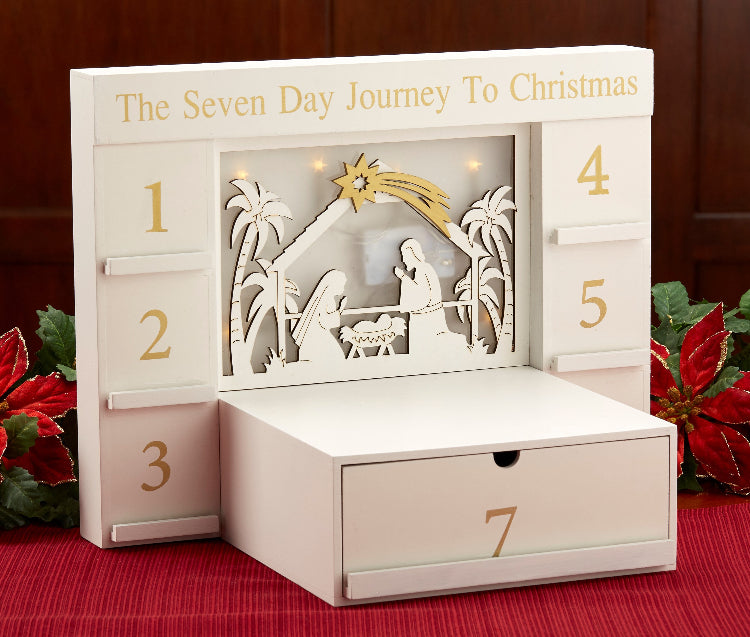 A white advent calendar with gold numbers and a nativity scene silhouette, titled 'The Seven Day Journey To Christmas', with a drawer for each day.
