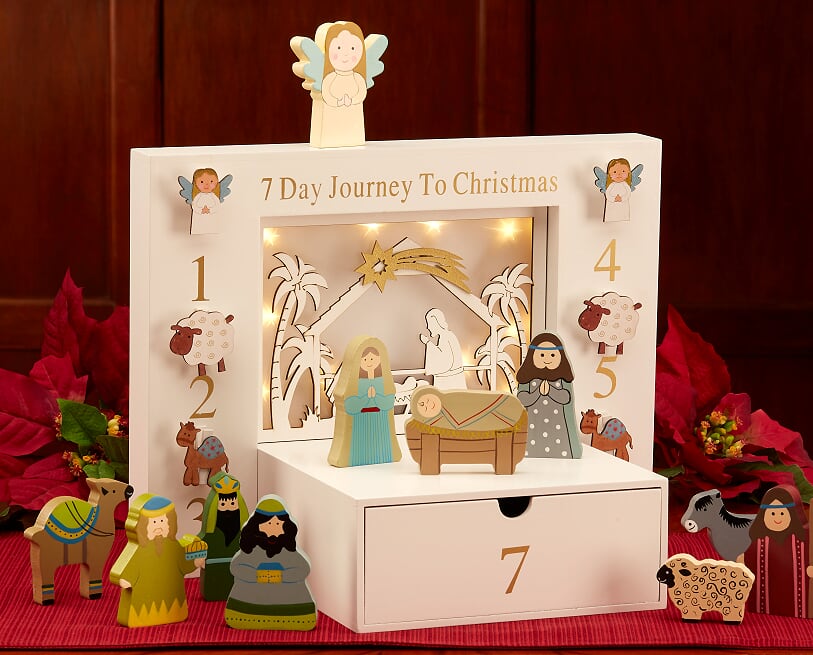 A children's nativity set depicting the nativity scene with figurines and a lighted centerpiece, placed on a red surface with decorative elements.