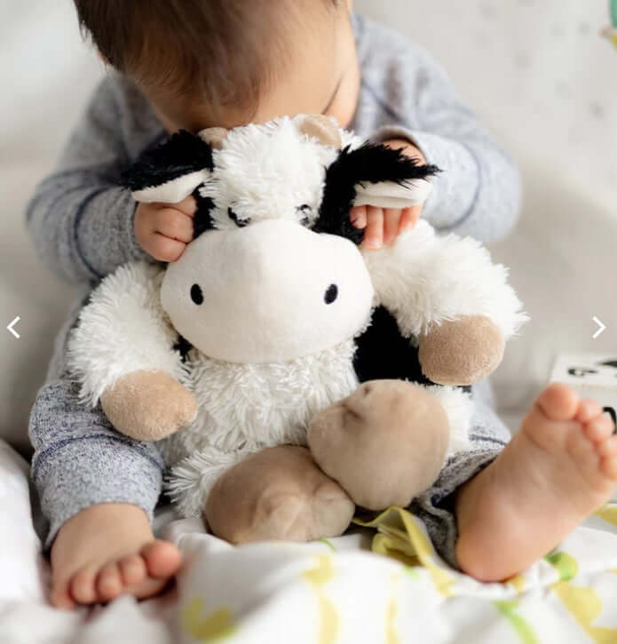 A child hugging a plush cow toy, showcasing why are Warmies so popular for comfort and companionship.