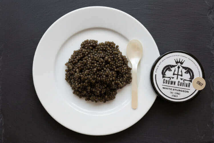 Premium Crown Caviar tin of Italian White Sturgeon roe served with blinis and crème fraîche on an elegant table setting