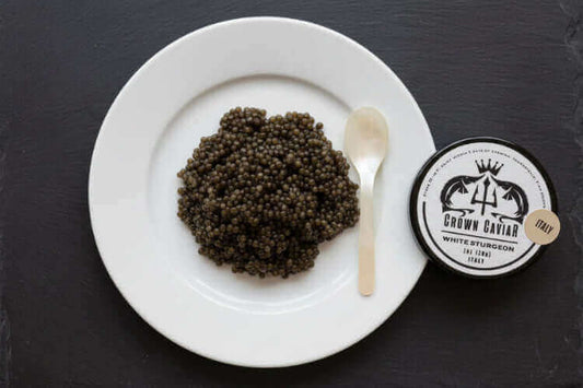 Premium Crown Caviar tin of Italian White Sturgeon roe served with blinis and crème fraîche on an elegant table setting