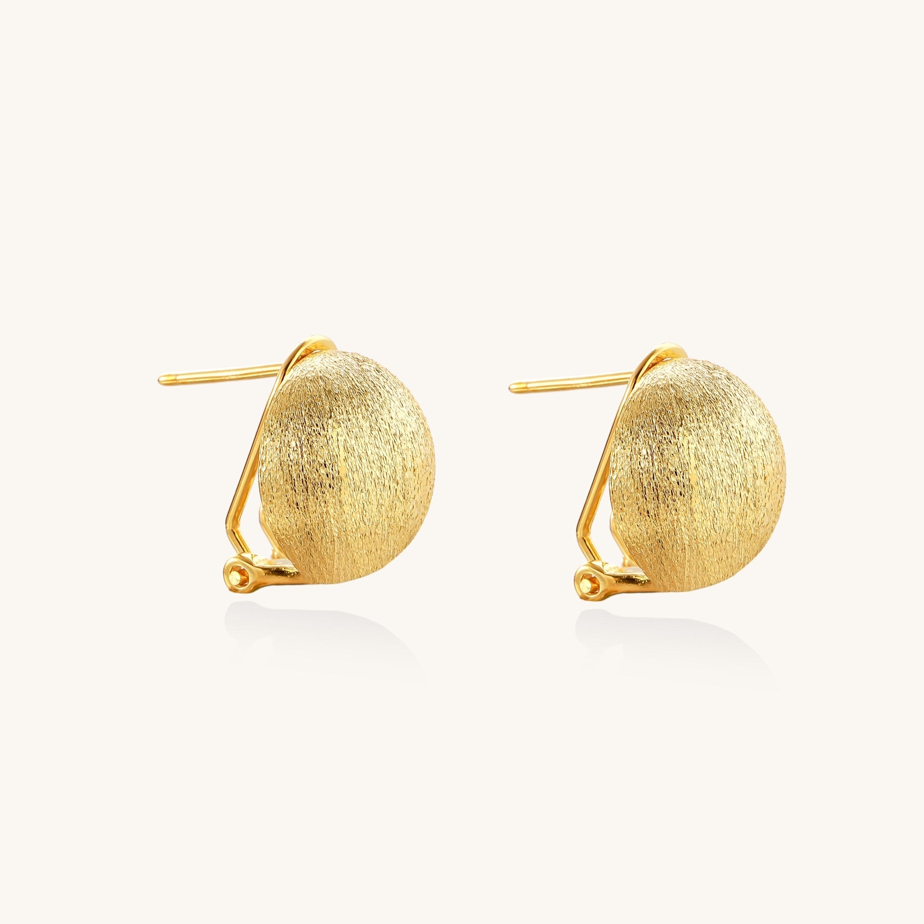 Close-up of textured gold-plated sterling silver dome clip-on earrings with brushed finish on white background.