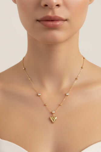 Dainty 14K gold plated necklace with heart pendant and bezel-set crystals on delicate chain against cream background.