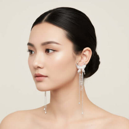Elegant silver-plated drop earrings with wing-shaped tops, white pearl accents, and long chain tassels on white background.