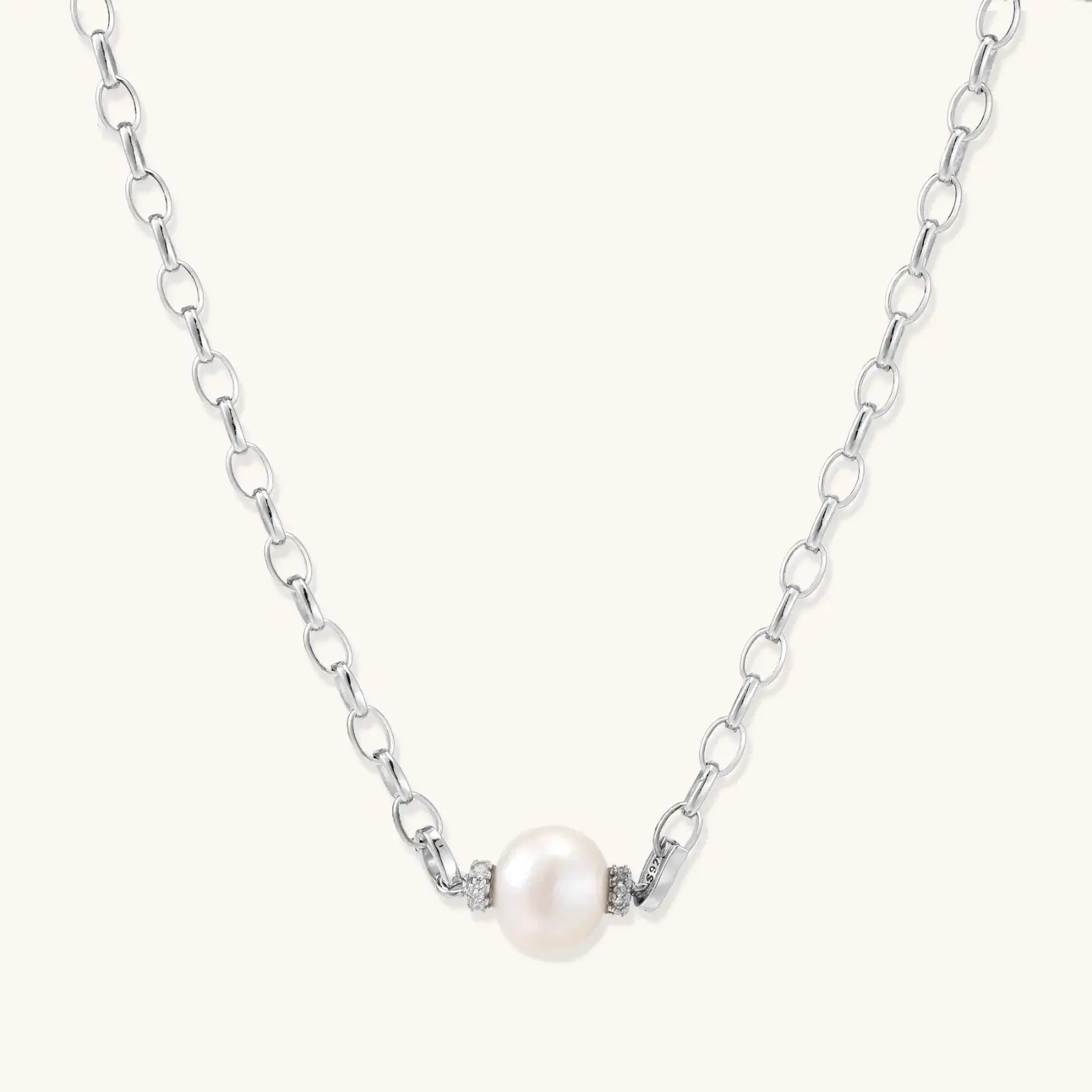 Dainty rhodium-plated silver chain necklace with centered 10mm freshwater pearl and crystal accents on cream background