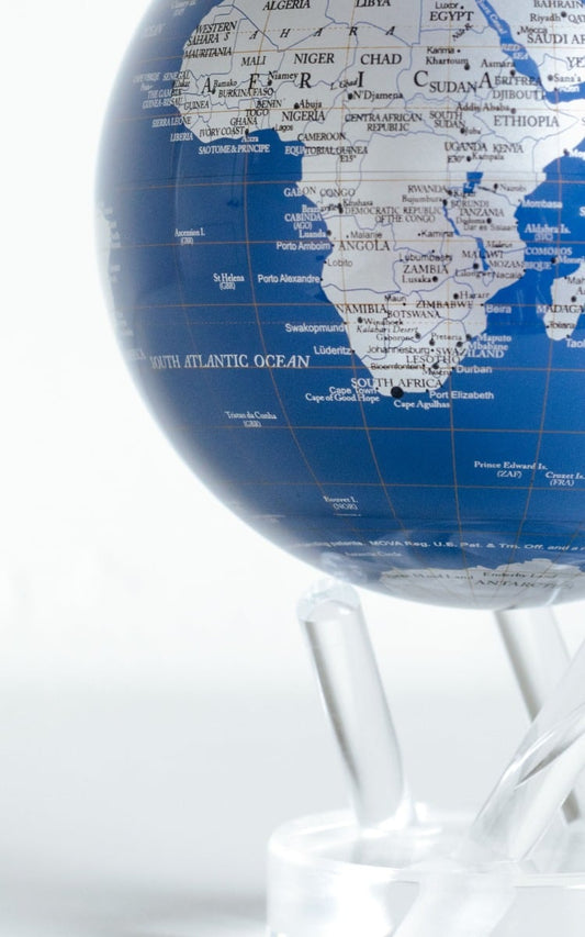 A rotating globe with silver landmasses on a blue background, set on a clear stand, demonstrating ambient light-powered technology.