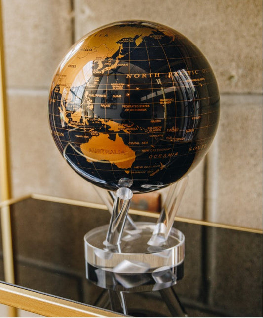 A black and gold MOVA Earth Globe with rotating gold landmasses on a jet-black ocean, displayed on a clear stand.