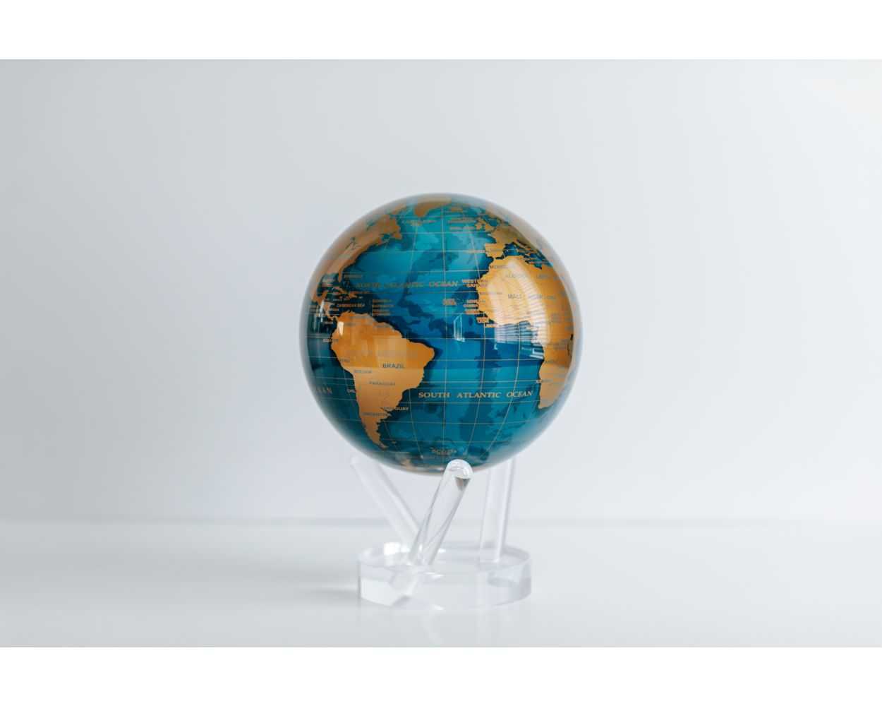 A contemporary rotating globe with cerulean blue oceans and gold metallic landmasses, powered by ambient light, displayed on a clear stand.