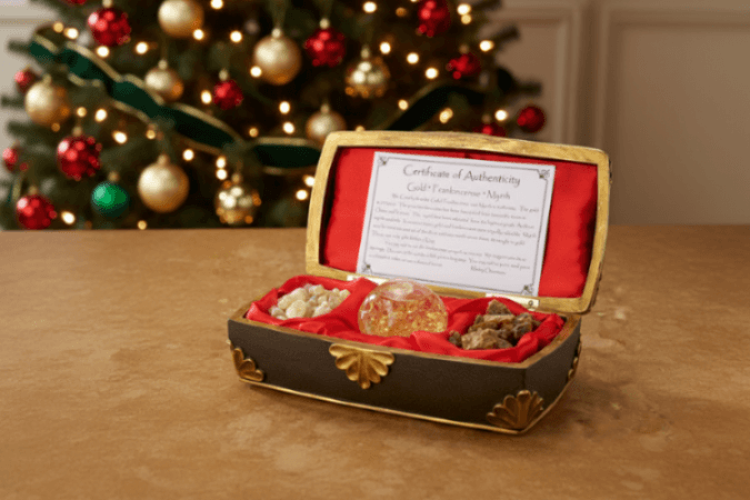 Decorative box with gold and red interior, containing small decorative items, on a wooden surface with a Christmas tree in the background.