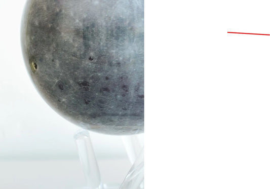 A rotating globe resembling the moon with a serene blue-grey color, displayed on a clear stand against a white background.