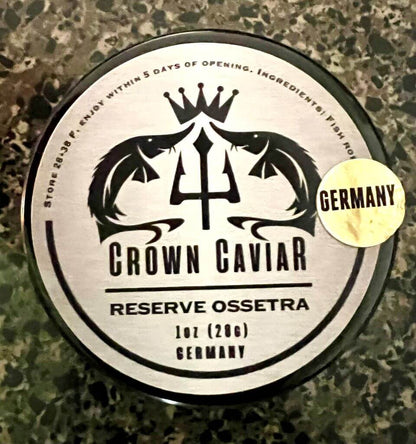A tin can labeled 'Crown Caviar Reserve Ossetra' with a weight indication of 1 oz (28g) and the text 'Germany'. The can is designed with a black and white color scheme featuring fish graphics, and there is a badge indicating 'Gourmet Selection'.