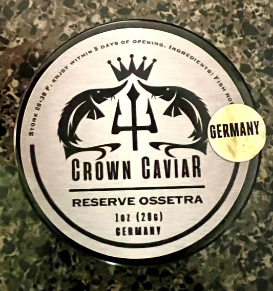 A tin can labeled 'Crown Caviar Reserve Ossetra' with a weight indication of 1 oz (28g) and the text 'Germany'. The can is designed with a black and white color scheme featuring fish graphics, and there is a badge indicating 'Gourmet Selection'.