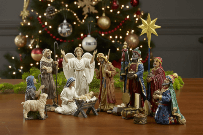 Nativity scene with figurines in front of a decorated Christmas tree.