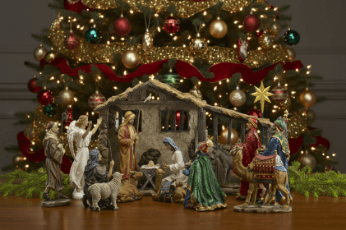 Nativity scene with figures in front of a decorated Christmas tree.