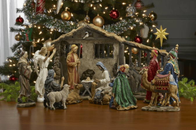 Nativity scene with figures in front of a decorated Christmas tree.
