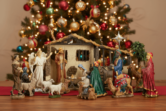 Nativity scene with figures in front of a decorated Christmas tree.