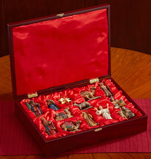 A 13-piece nativity ornament set displayed in a satin-lined wooden storage box with gold foil stamping, opened on a wooden surface.