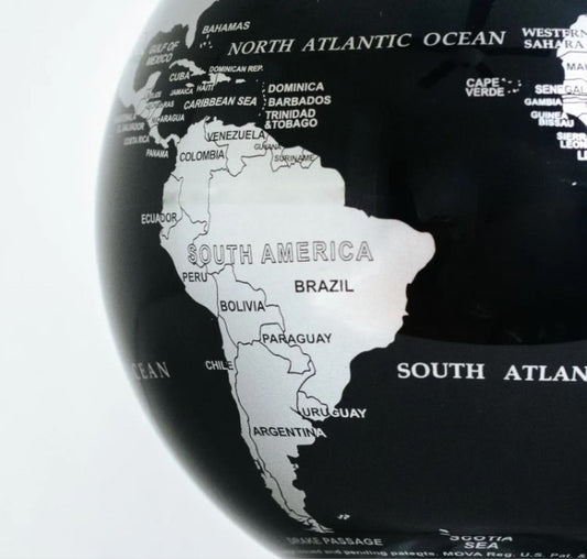 A black and silver MOVA Earth globe with metallic silver landmasses on a deep black ocean, displayed on a clear stand.