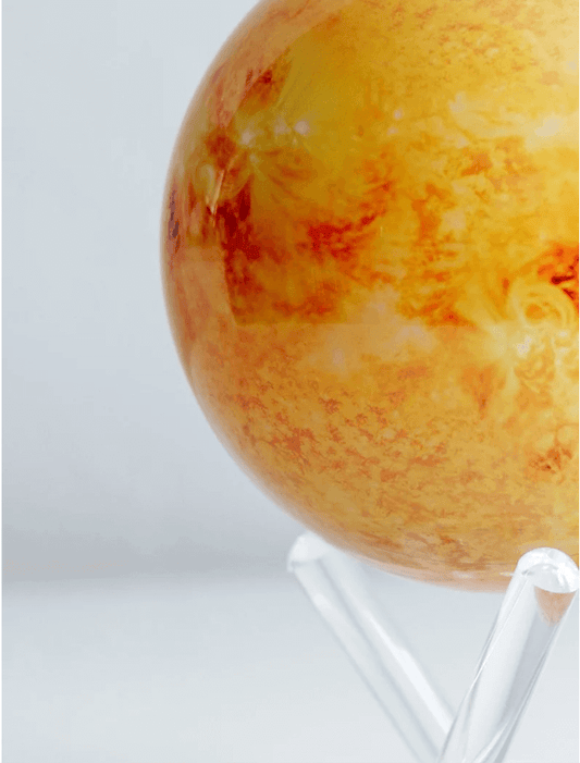 A rotating globe model representing the Sun, displayed on a stand, featuring a detailed yellow surface with red and orange hues.