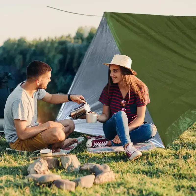 Outdoor Emergency Survival Tent and Blanket used by two people enjoying a drink outdoors, with a tent in the background.