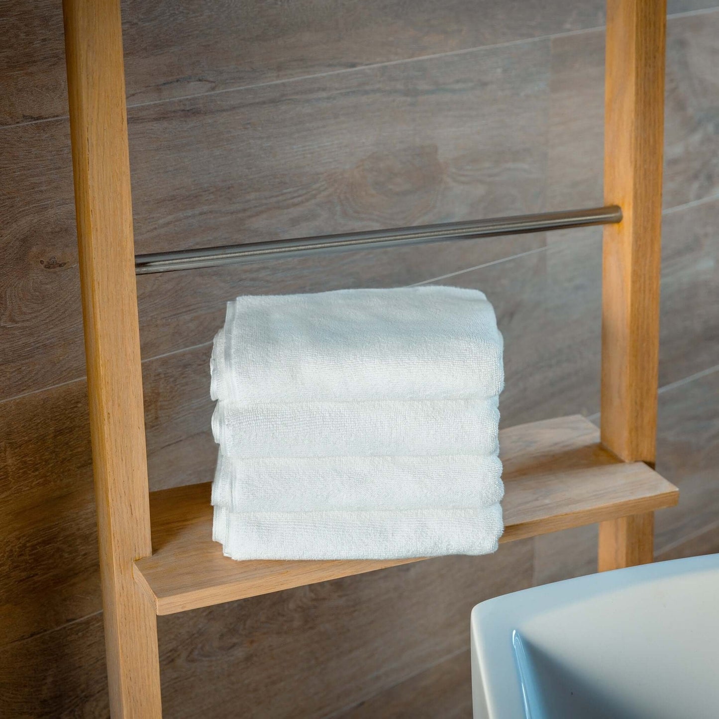 Four neatly stacked white towels on a wooden shelf in a modern bathroom, perfect for enhancing luxury organic bath mats.