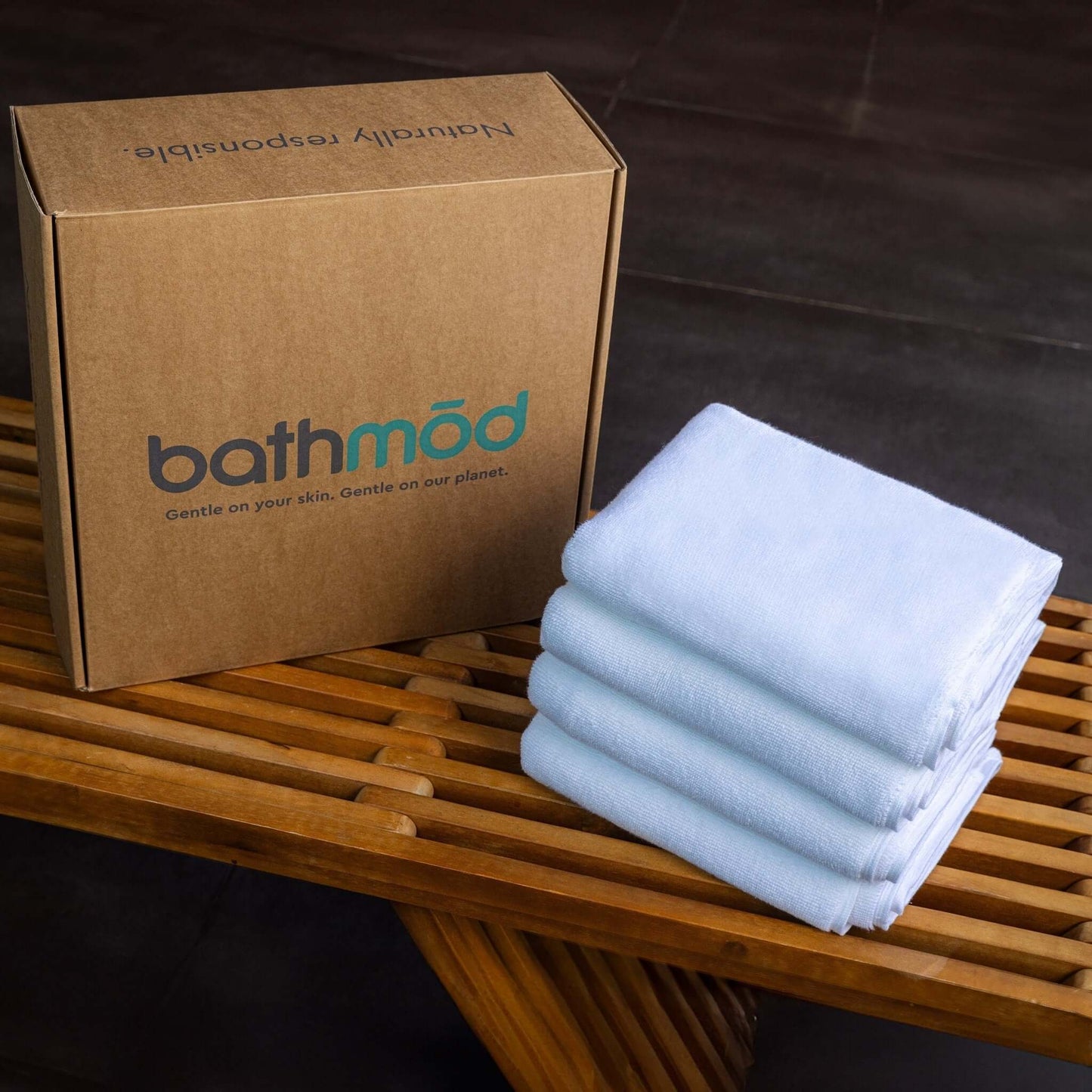 Luxury organic bath mats four-pack displayed beside a brown box on a wooden surface.