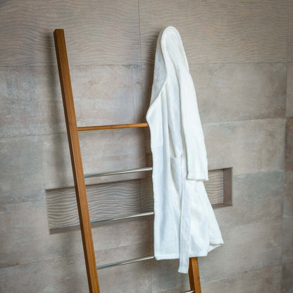 Luxury organic bathrobe hanging on a wooden ladder against a modern, textured wall.