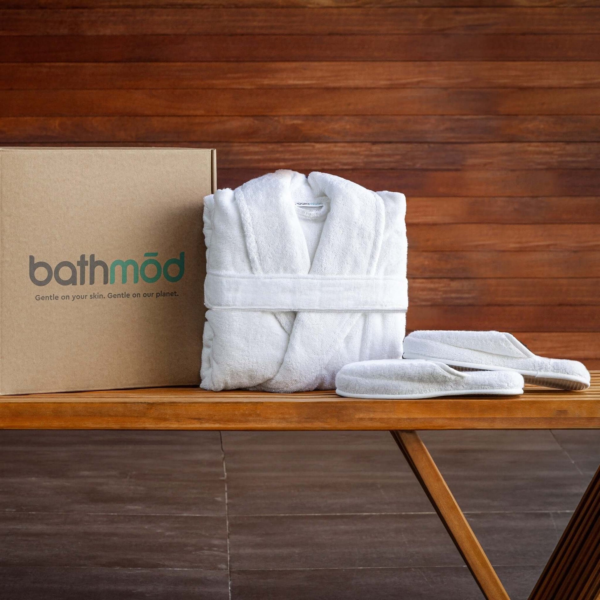 Luxury organic bathrobe and slipper set displayed on a wooden table beside its eco-friendly packaging.