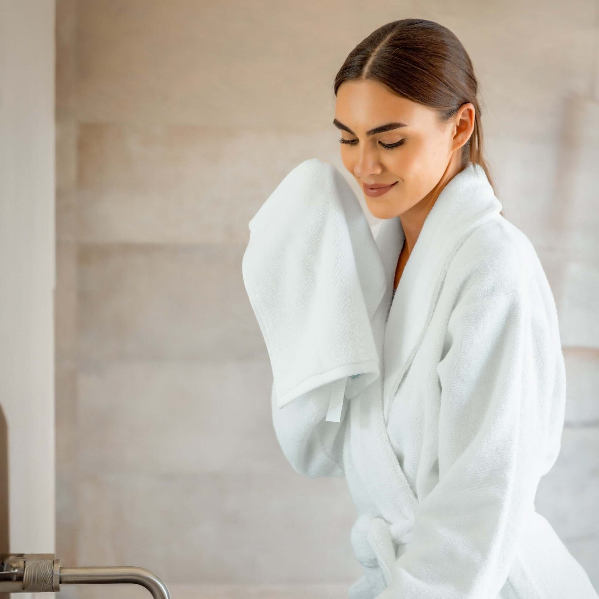 Woman enjoying a luxurious experience in a luxury organic bathrobe, gently holding a towel.