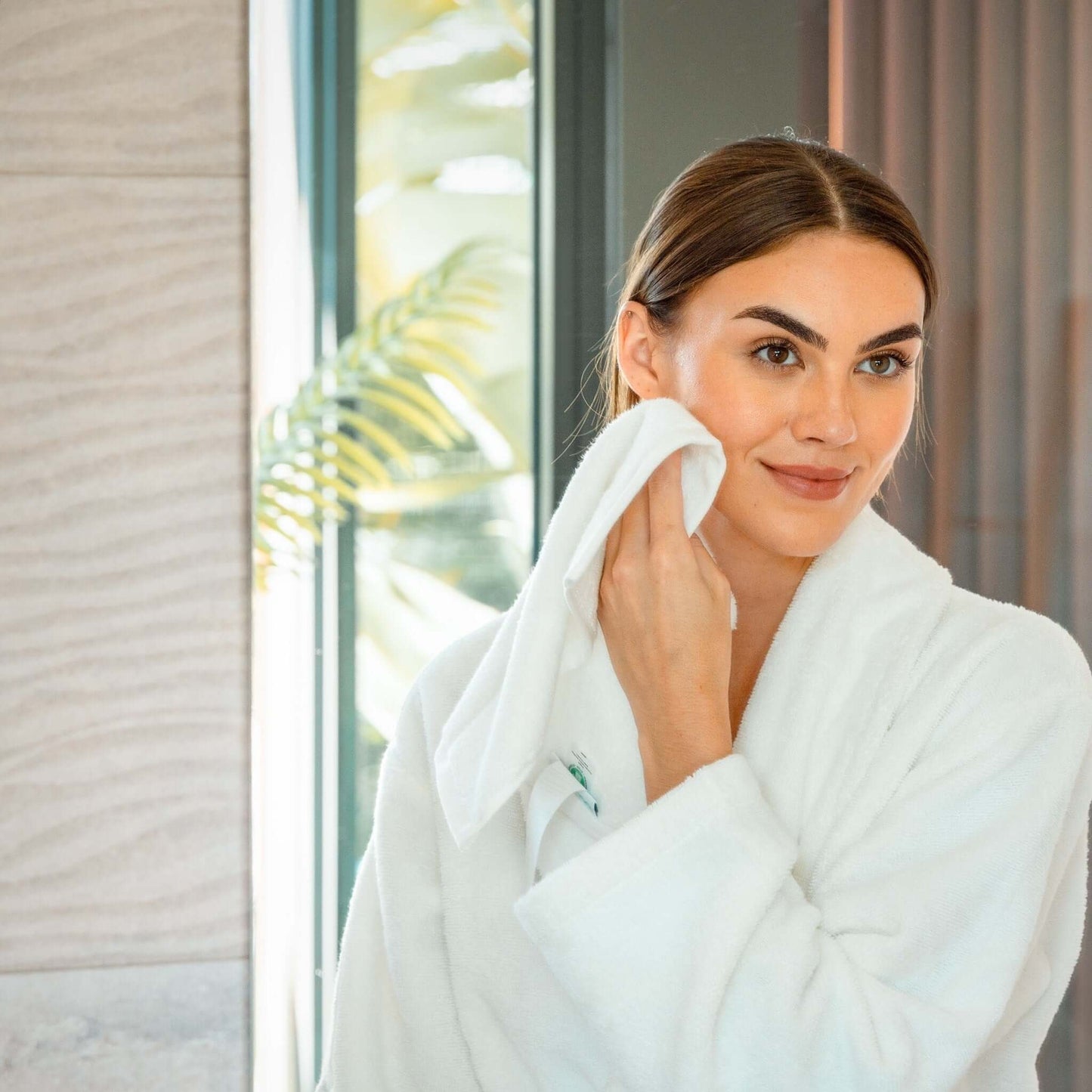 Woman in a plush robe using a luxury organic bath towel set, demonstrating softness and comfort.