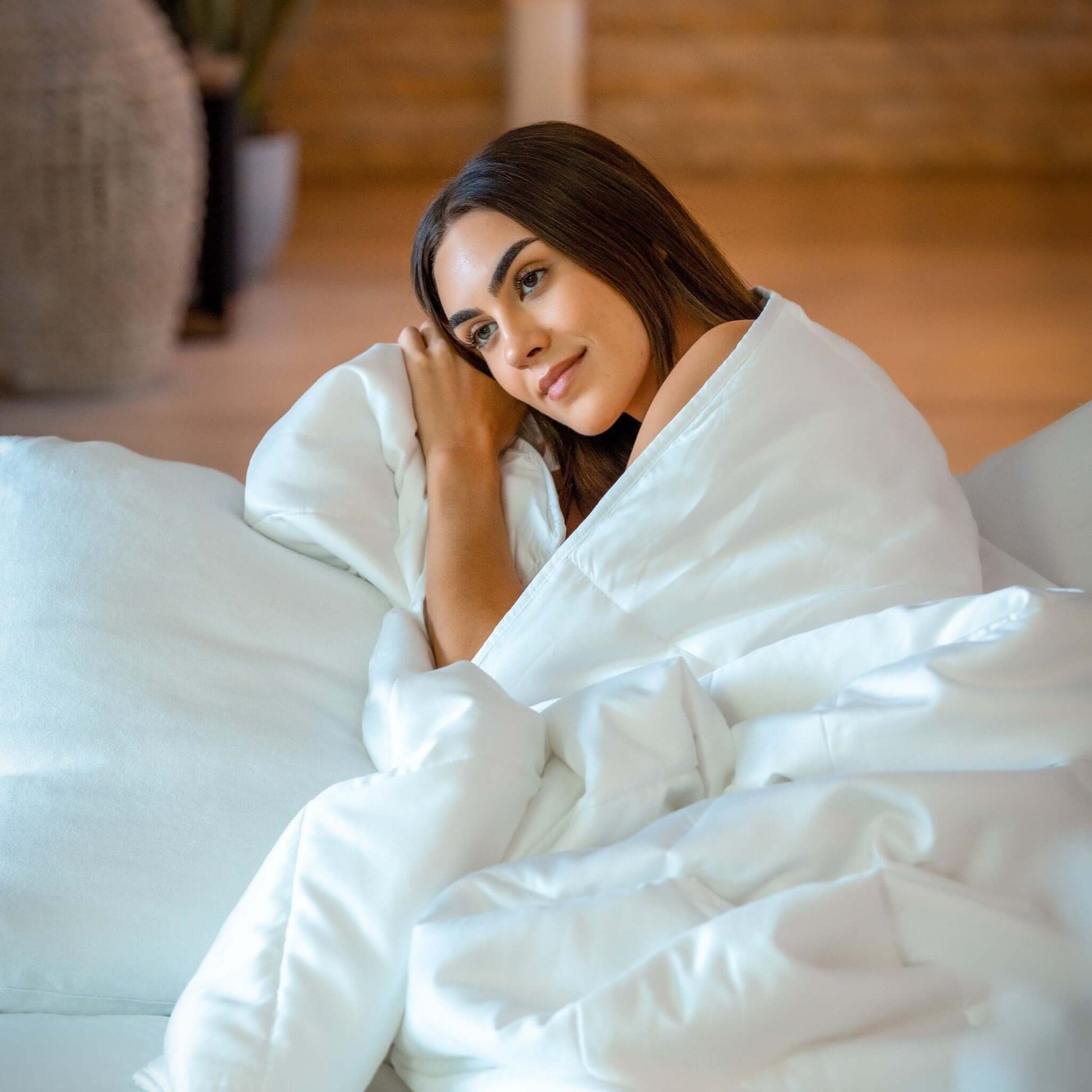 Woman relaxing on a couch, cozy under a temperature regulating eucalyptus silk comforter set.