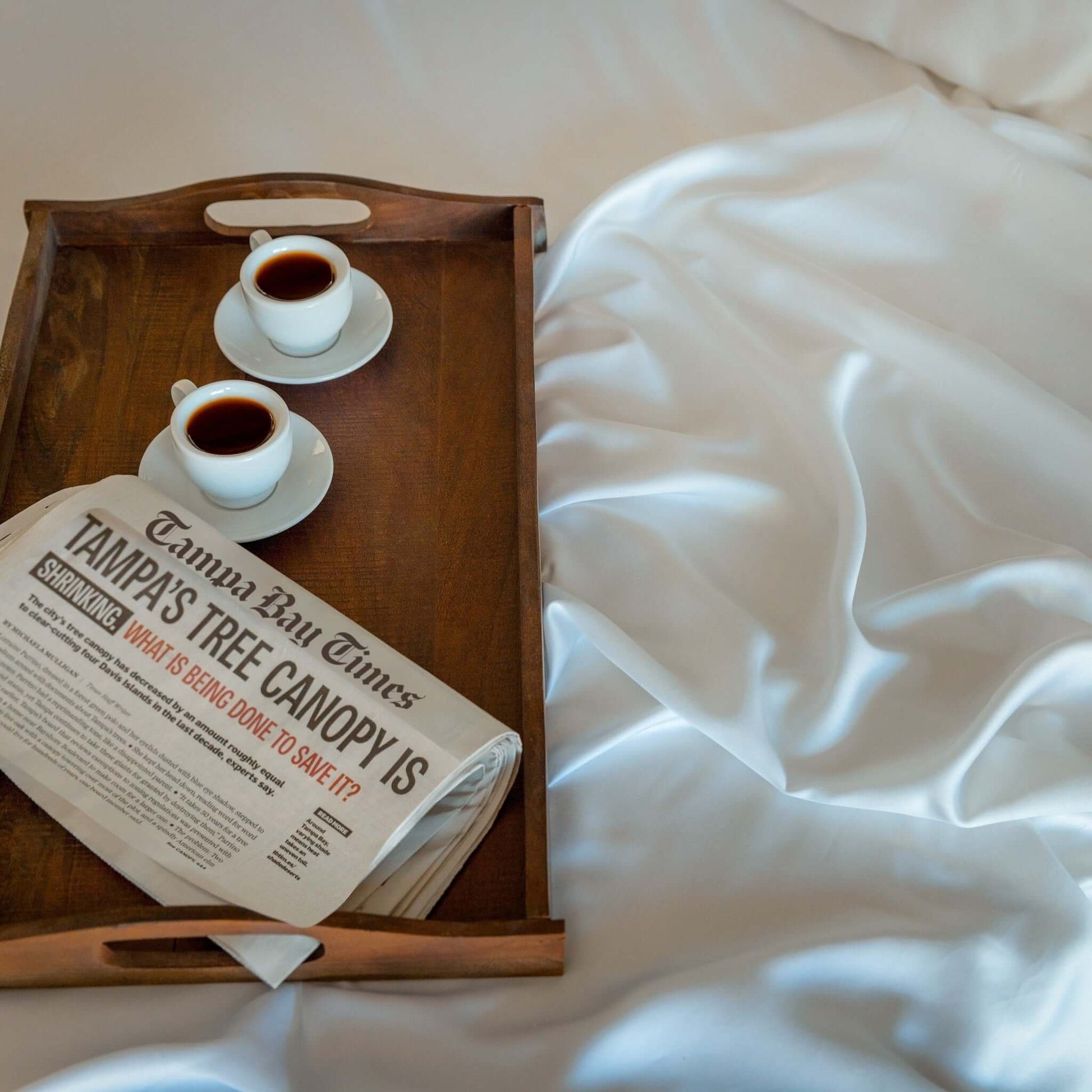 Eucalyptus silk sheets displayed with coffee cups and a newspaper on a tray, highlighting their luxurious softness.