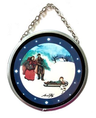 A round stained glass Christmas ornament featuring a vintage winter scene with a sleigh ride, two figures, and a child on a sled, with a chain for hanging.